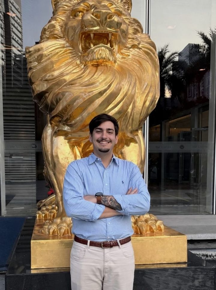 Pedro Paulo Angarita em viagem de negócio, diante de uma escultura de leão dourado